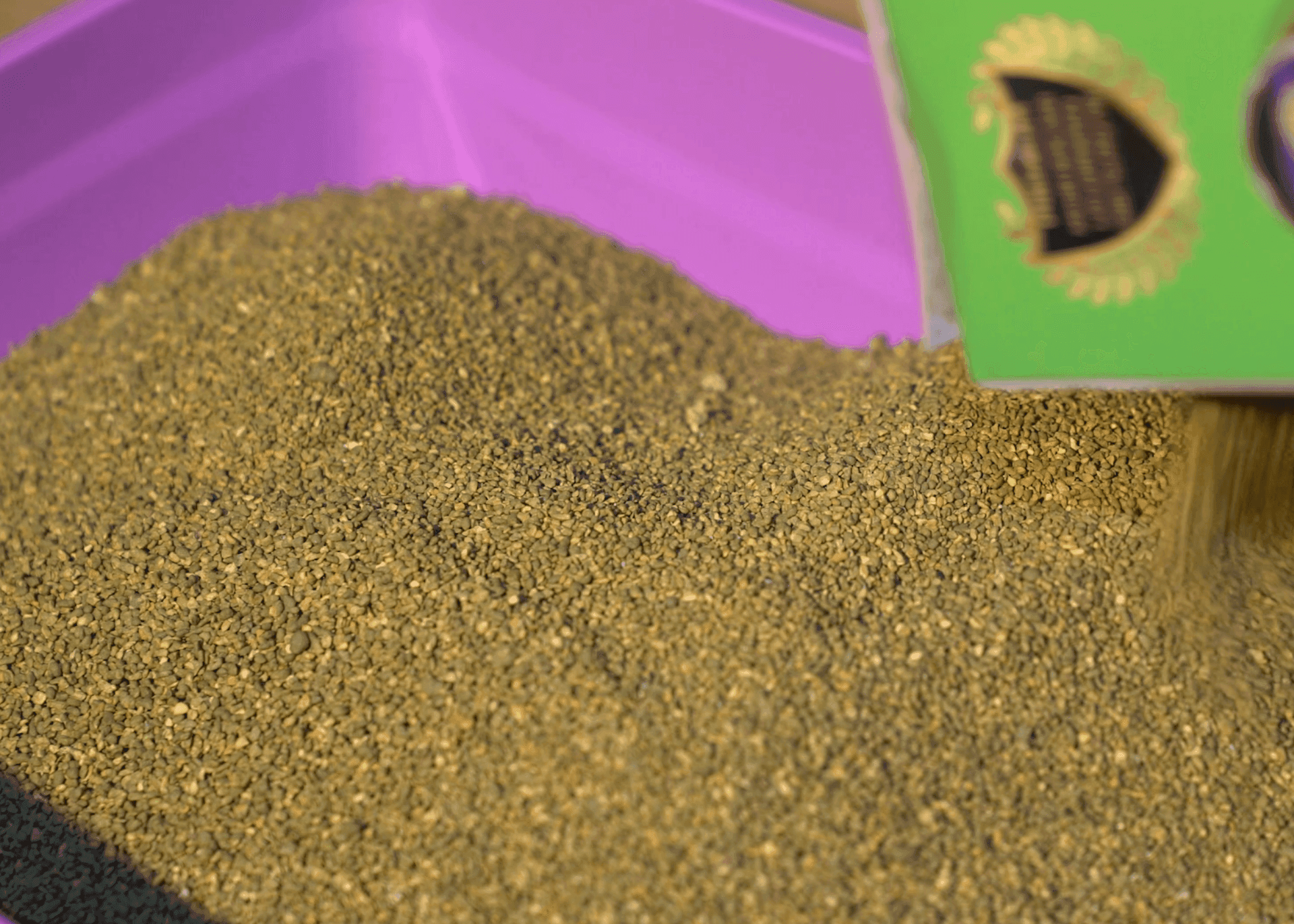 Granular material being poured into a purple container from a green box.